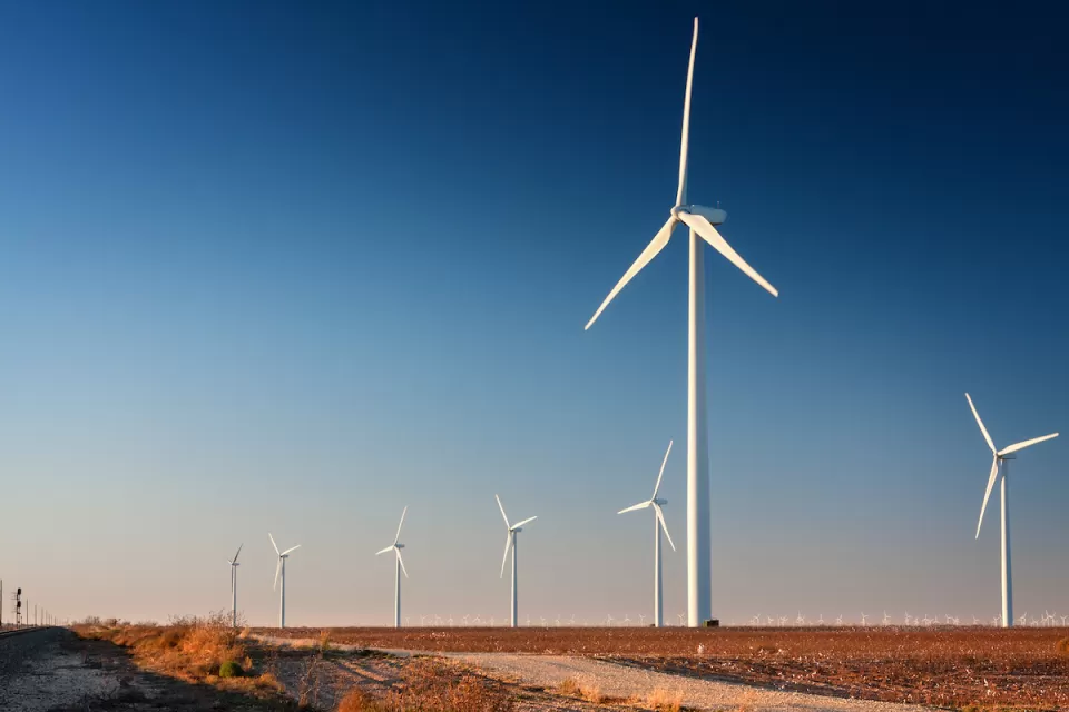 Row of white wind turbines in wide open dirt field in west Texas.